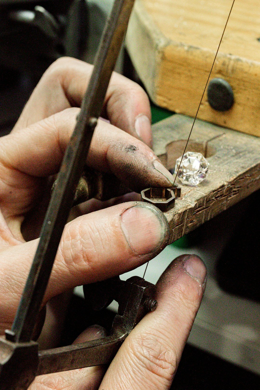 Hands using a saw to cut a gold setting, with a white topaz stone on the peg behind it.